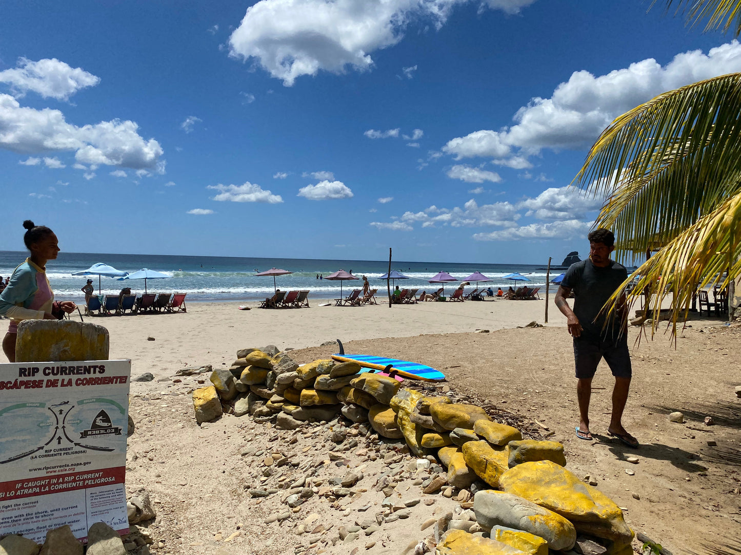 San Juan Del Sur beach with chairs, umbrellas, and a rip current sign.