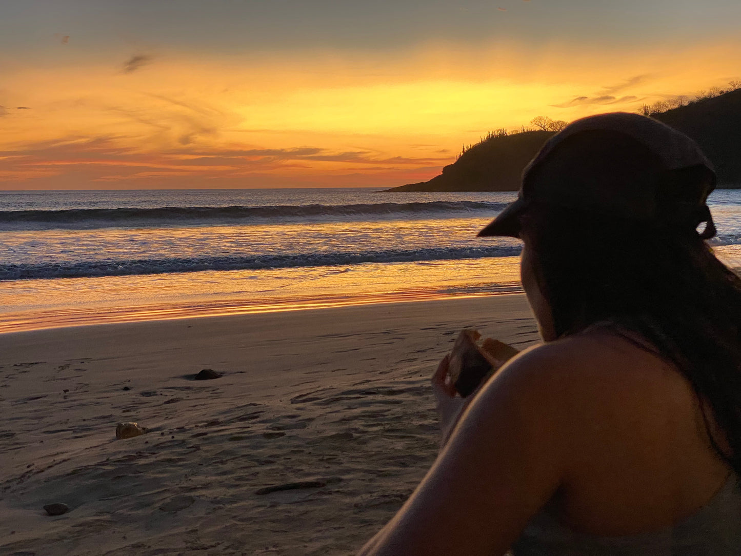 Girl wearing a cap eating a sandwich during a yellow sunset in San Juan Del Sur.