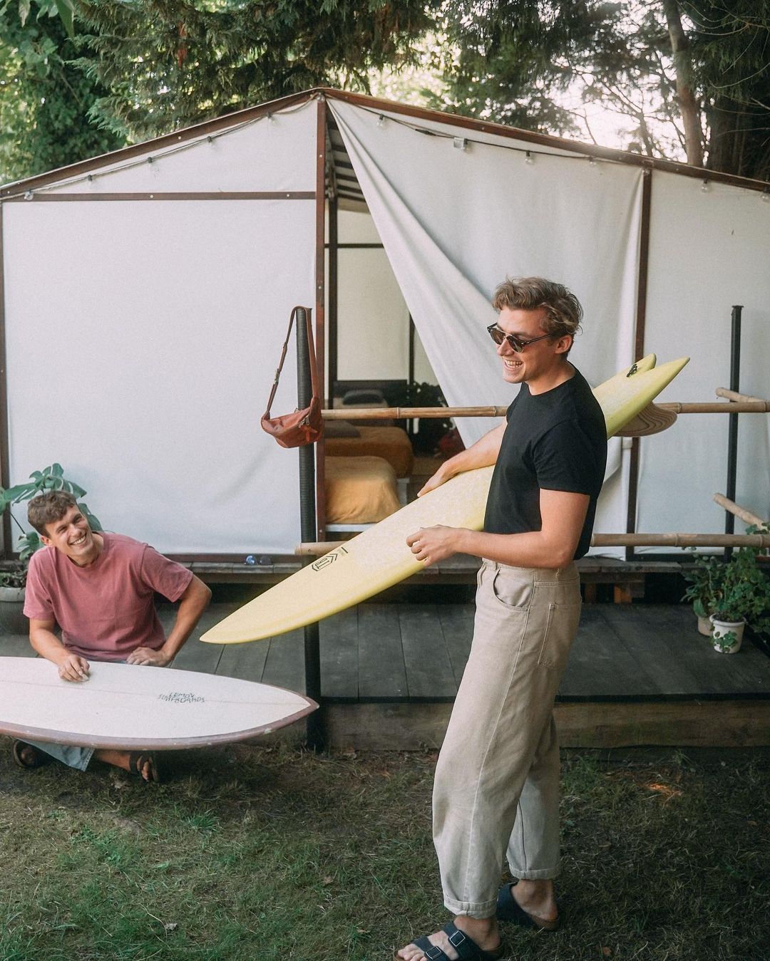 Two guys laughing while holding surf boards at their small group travel accommodation in Cantabria.