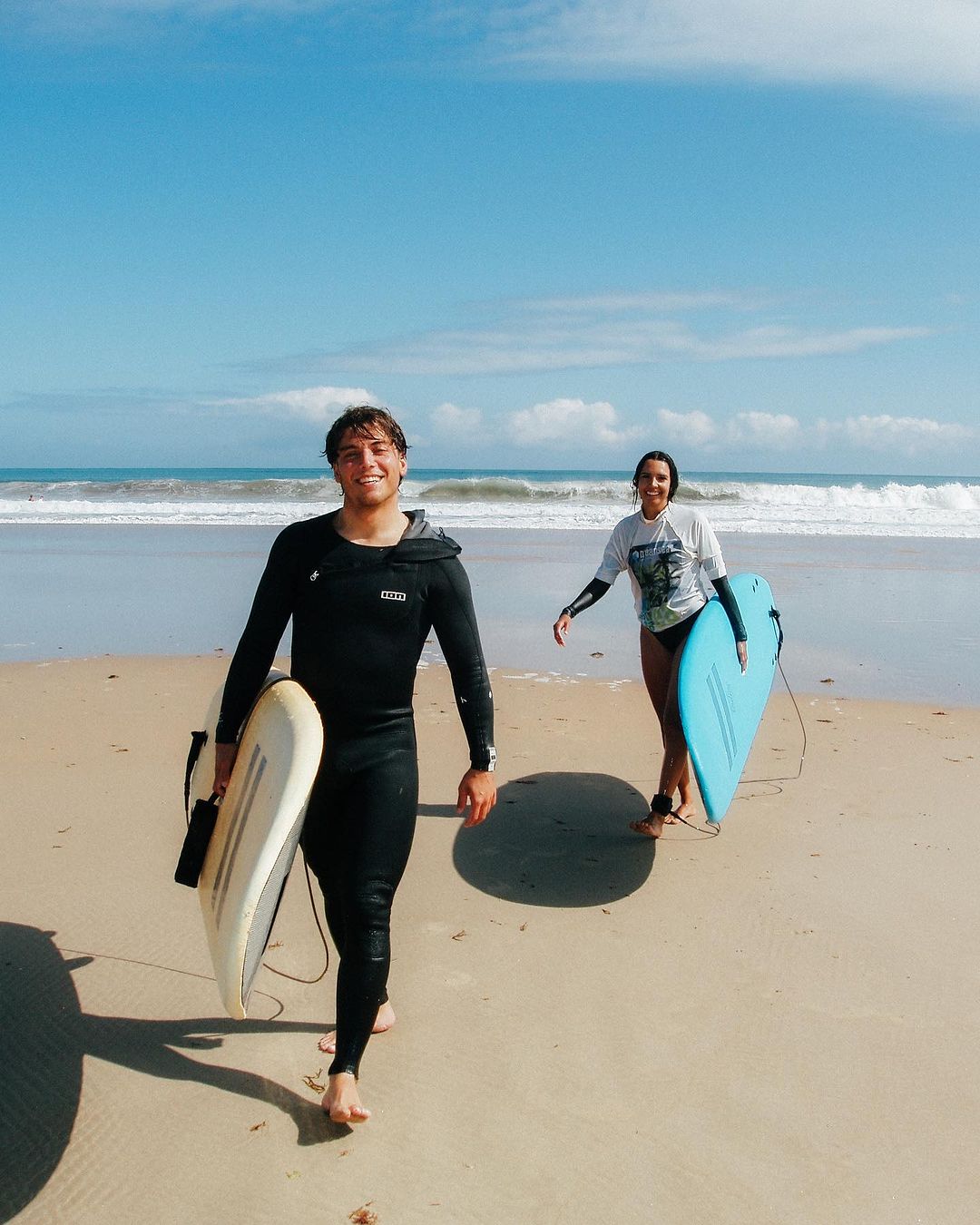Two smiling surfers leaving the beach in Cantabria after their group surf lessons.