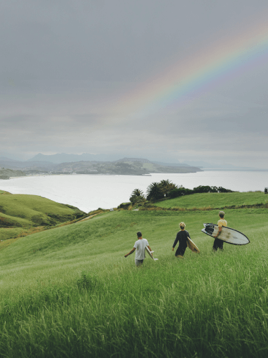 Surfers walking through a field under a rainbow during a small group trip excursion in Cantabria.
