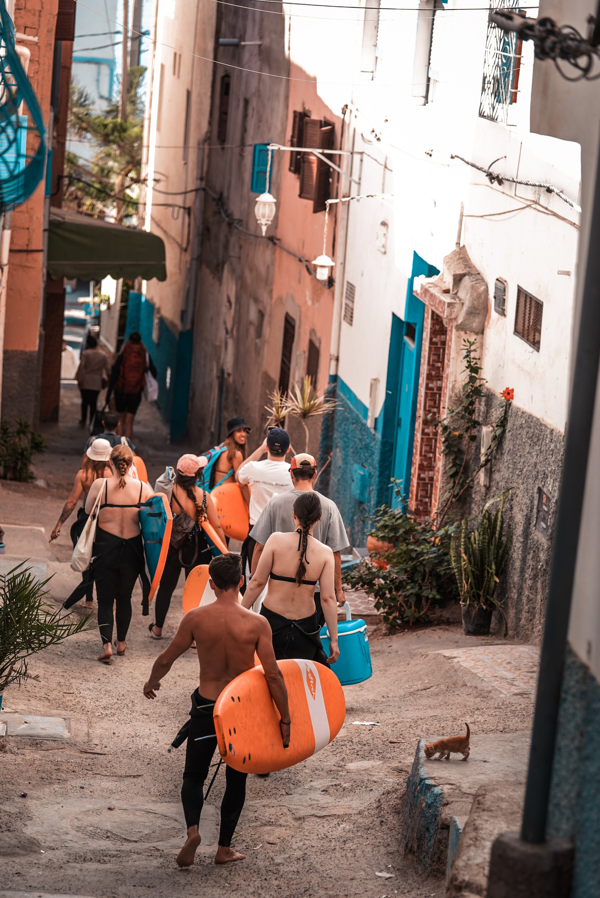 Small group trip participants carrying their surfboards down a small street in Taghazout.