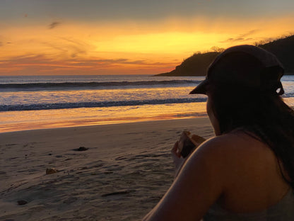 Girl wearing a cap eating a sandwich during a yellow sunset in San Juan Del Sur.