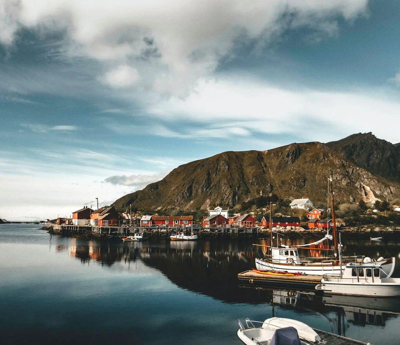 Fishing boats parked on the water in Ballstad Norway near a big mountain.