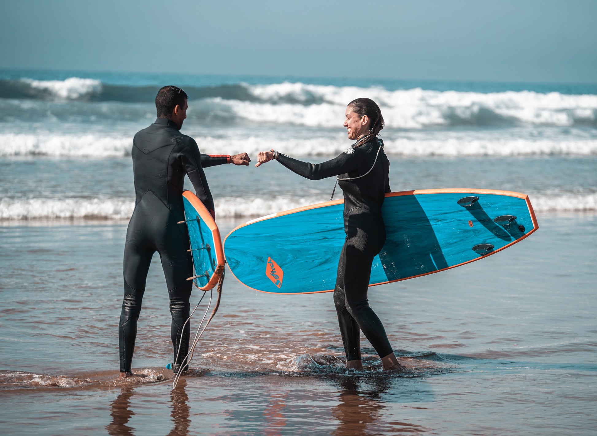 Two surfers fist bumping while holding their surf boards in Taghazout during a small group trip.