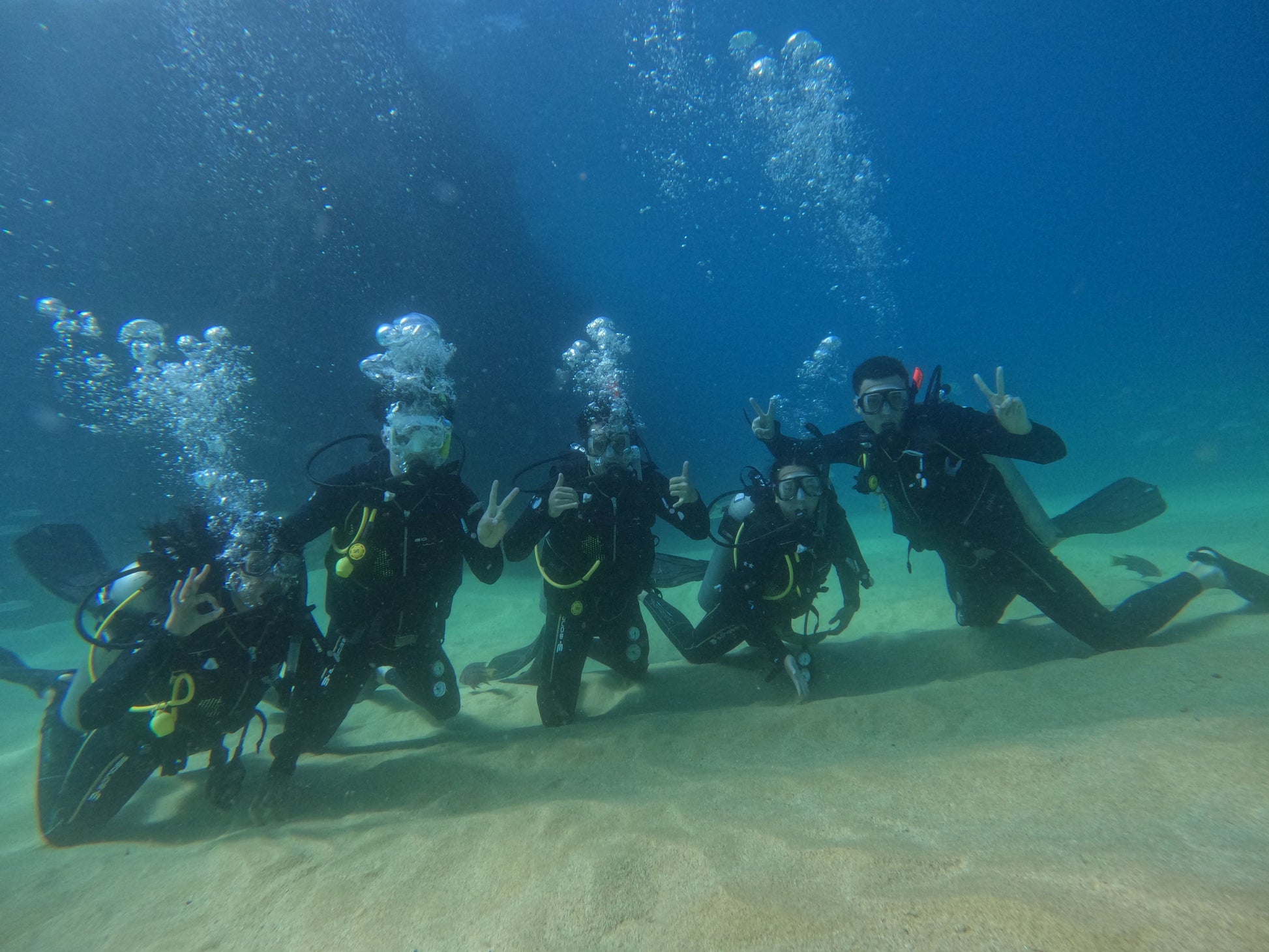 Small group trip participants scuba diving in Los Cabos holding up peace signs underwater.