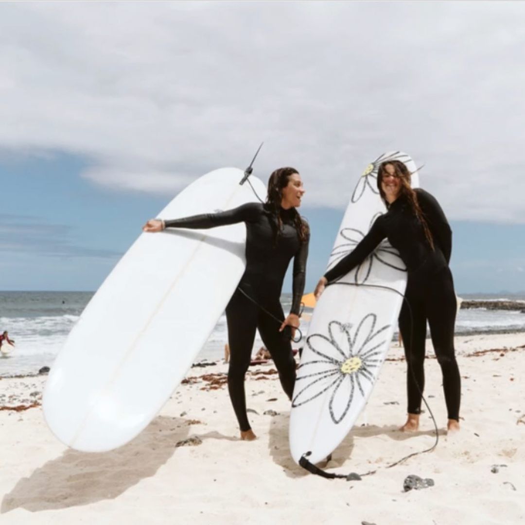 Two girls carrying surf boards on the beach during a Fuerteventura small group trip.