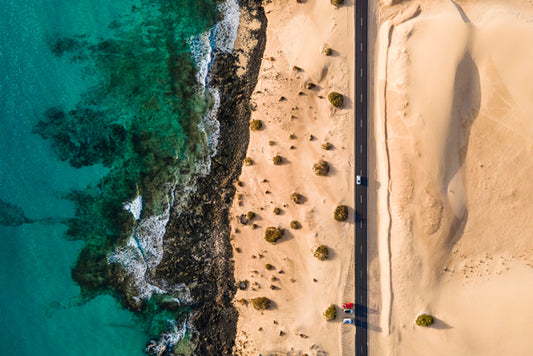 Aerial view of a one lane highway between the ocean and sand in Fuerteventura.