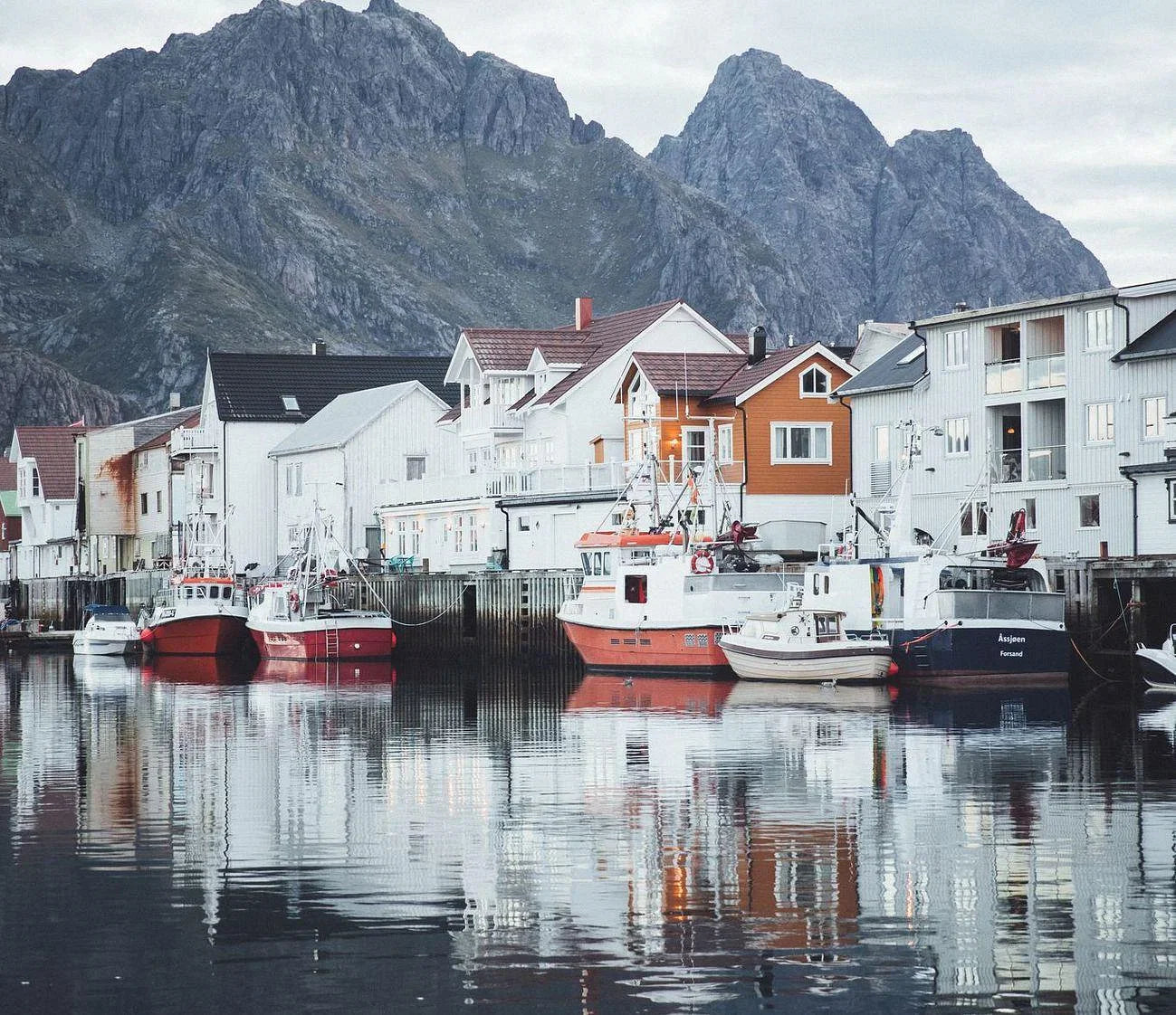 Houses above the water in Henningsvaer Norway with boats parked near them.