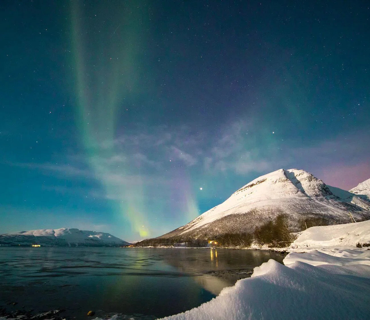 Northern lights in the sky above the water and snowy mountains in Tromso Norway on a small group trip.