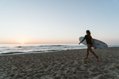 Small group trip participant with surfboard in hard walking towards the ocean in Portugal at sunset.