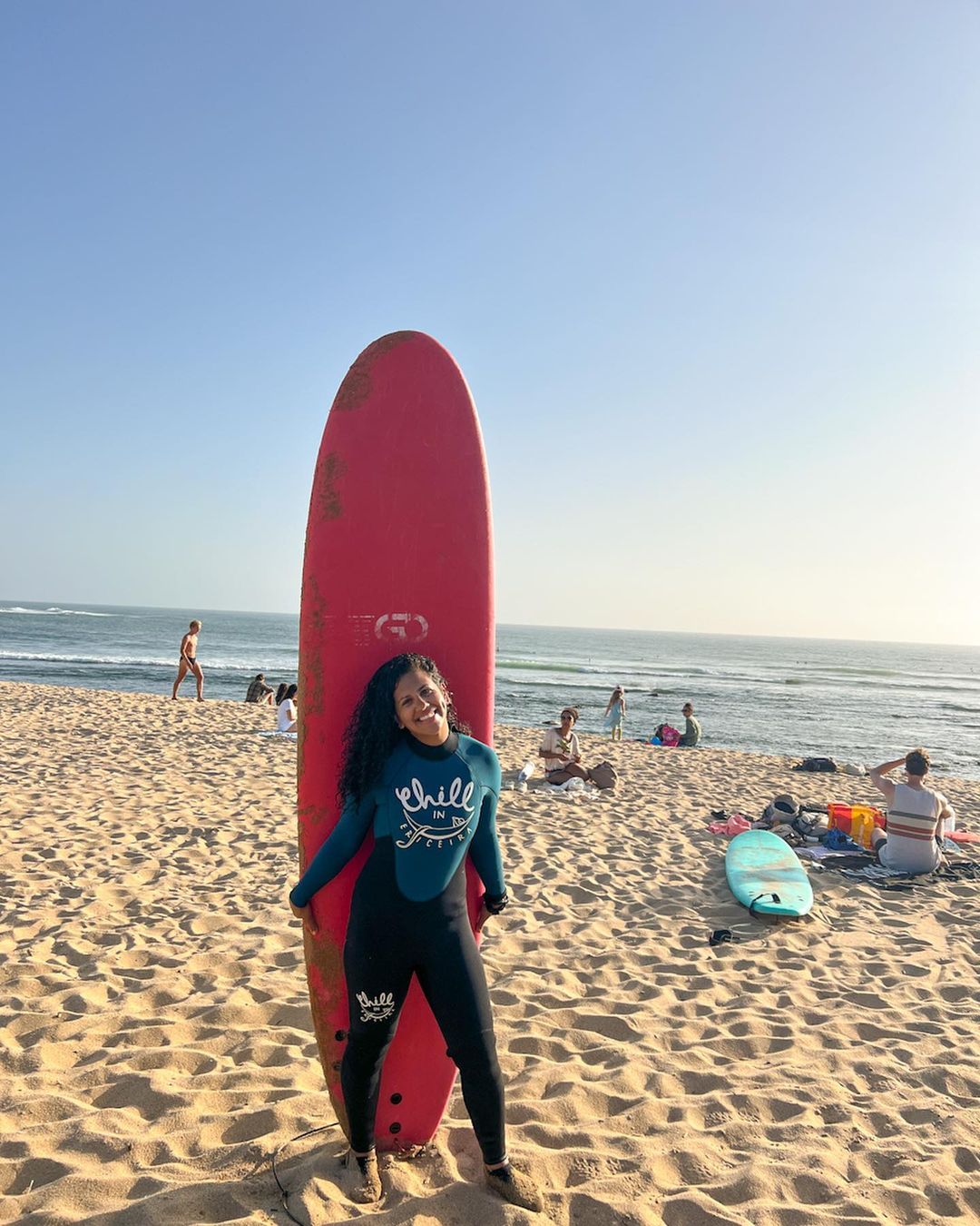 Trip leader Christina Patel holding her surfboard on the beach of Taghazout.