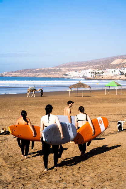 Trip participants walking along the sand with their surf boards preparing for surf lessons in Morocco.