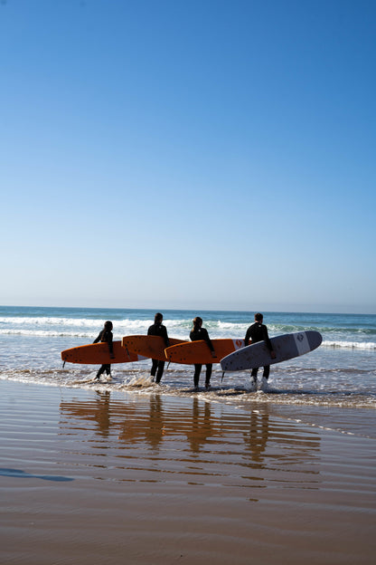 Four small group trip participants walking into the Moroccan ocean with their surf boards in hand.